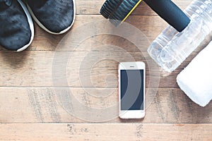 Flat lay of mobile phone with sport equipments on wood background. Woman sneaker with abs equipment