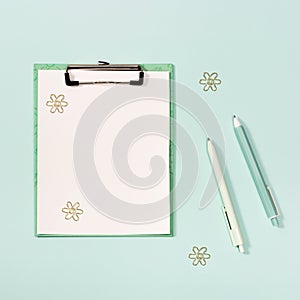 Flat lay with mock-up paper tablet with clip, blue and white colored pens, metal paperclips.