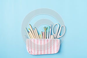Flat lay of modern bright blue office desktop with school supplies on table around empty space for text in pencil case