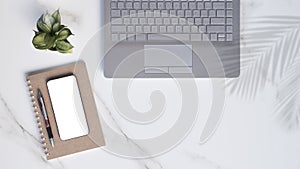 Flat lay of modern white marble office desk table with laptop, smartphone mock up, ballpoint pen, spiral notebook with little