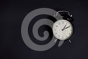 Flat lay. Monochrome composition with a vintage alarm clock on black background with copy space to add text. Back to School and