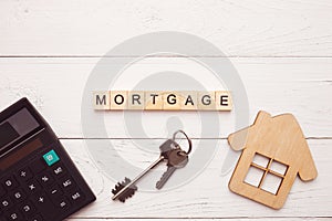 Flat lay of mortgage concept. Calculator, wooden house and keys on a white wooden background