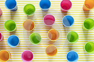 Flat lay of multi-colored plastic cups on a yellow background. Concept items for fast food. Top view