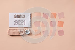 Flat lay of notepad with words Goals 2021, colorful sticky notes, o`clock, pen and pen case. Color pink background
