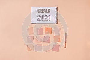 Flat lay of notepad with words Goals 2021, colorful sticky notes, o`clock, pen and pen case. Color pink background