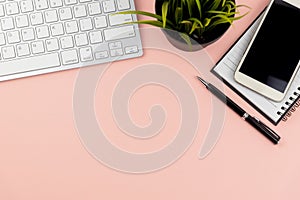 Flat lay office desk with computer keyboard, smart phone, pen, note pad and potted plant