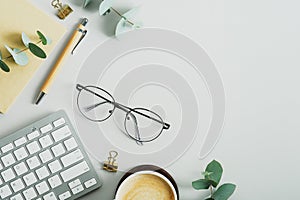 Flat lay office desk table with glasses, computer keyboard, paper notebook, pen, eucalyptus branches. Elegant feminine workspace,