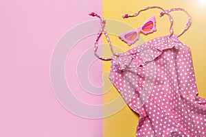 Flat lay ofPink dress and pink sunglasses on pink and yellow background. Top view, flat lay. Summer clothes set. Girl`s dress set