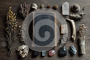 Flat lay of an old spellbook, dried herbs, crystals, and carved bone talismans on a wooden table photo