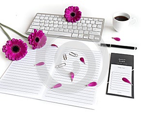 Flat lay: open notebook, keyboard, coffee, black pen and pink, purple, violette, red Gerbera flower with petals photo