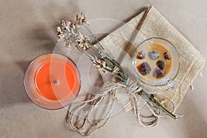 Flat lay of orange candle, cup of iced coffee and dried flowers