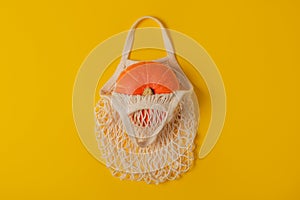 Flat lay orange pumpkin in reusable mesh string bag on yellow background. The concept of Halloween, Thanksgiving. Zero waste