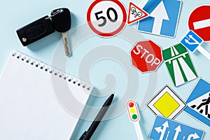 Flat lay paper notebook, car keys, road sign on blue background. Driving school concept