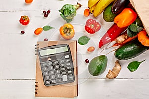 Flat lay paper shopping bag with assortment of fresh vegetables and fruits and calculator