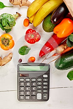 Flat lay paper shopping bag with assortment of fresh vegetables and fruits and calculator