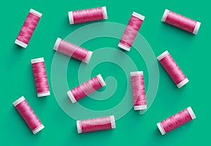 A flat lay pattern of spools of pink thread on green background. Top view