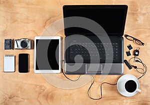 Flat lay of personal office accessories, laptop, notebook, coffee cup and camera on wood background, top view