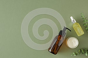Flat lay photo of amber pump bottle without label, dropper bottle, cream jar and eucalyptus leaves on pastel green background