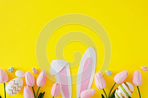 Flat lay photo with bunny rabbit ears, tulips flowers and color eggs on yellow background