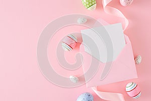 Flat lay photo of colorful eggs, envelope with letter and satin ribbon on pastel pink background