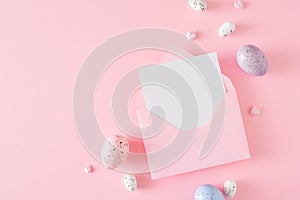 Flat lay photo of colorful eggs, open envelope with white card on pastel pink background