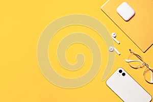 Flat lay photo with a copy space on the left side, and objects on the right: white smartphone, wireless earphones with a charging