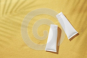 Flat lay photo of cosmetic bottles without label, green tropical leaves and shadow on sandy background