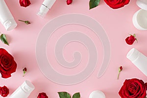 Flat lay photo of cosmetic bottles, red roses, green leaves on pastel pink background