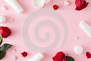 Flat lay photo of cosmetic bottles, red roses and hearts on pastel pink background