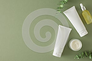 Flat lay photo of cosmetic tubes without label, dropper bottle, cream jar and eucalyptus leaves on pastel green background