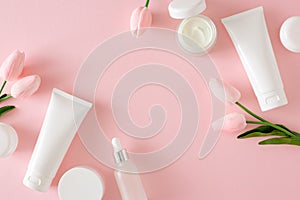 Flat lay photo of cosmetic tubes without label, serum bottles, cream jars and spring flowers