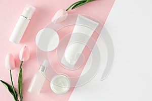 Flat lay photo of cosmetic tubes without label, serum bottles, cream jars and spring flowers