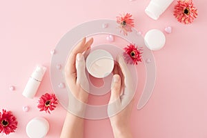 Flat lay photo of cream jar in hands, heart shaped candles, cosmetic bottles and flowers