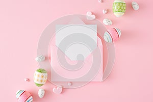 Flat lay photo of Easter eggs, envelope with card and hearts baubles on pastel pink background