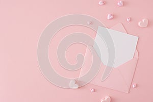 Flat lay photo of envelope with letter and pink heart shaped baubles on pastel pink background