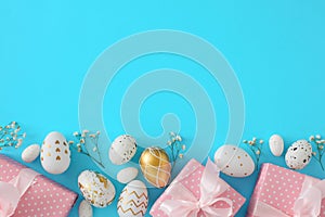 Flat lay photo of gift boxes with ribbons, white gold eggs, gypsophila flowers on pastel blue background