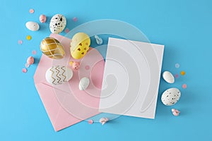 Flat lay photo of gold, white, shiny eggs, cute rabbits, envelope with white card and confetti