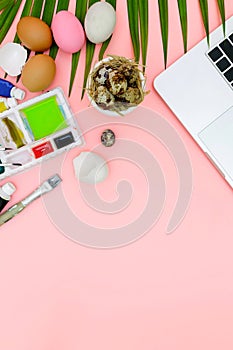 Flat lay photo of modern workplace with laptop and eggs, top view laptop background and paint set preparing for Easter on pink
