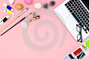 Flat lay photo of modern workplace with laptop and eggs, top view laptop background and paint set preparing for Easter on pink