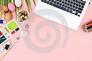 Flat lay photo of modern workplace with laptop and eggs, top view laptop background and paint set preparing for Easter on pink