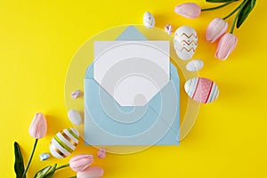 Flat lay photo of multicolored eggs, spring flowers, cute easter bunnies on yellow background