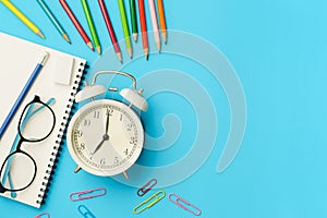 Flat lay photo of office desk with colorful pencil, Paper clip, Glasses, Note book, White retro clock, Top view of the copy space