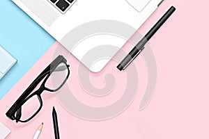Flat lay photo of office desk with tablet, laptop, pencil and pen, cactus, glasses, pink and blue background