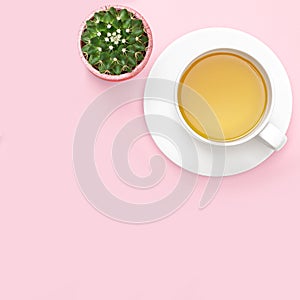 Flat lay photo of office desk with tea mug, cactus, pink background