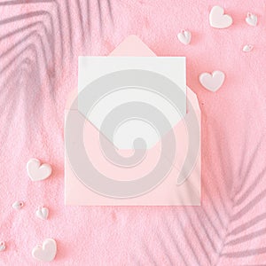 Flat lay photo of open envelope with white card, hearts baubles and tropical leaf shadows