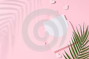 Flat lay photo of open envelope with white card, hearts, palm leaf and tropical leaf shadow