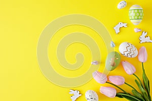 Flat lay photo of open envelope with white card, spring tulips flowers and cute easter bunnies on yellow background