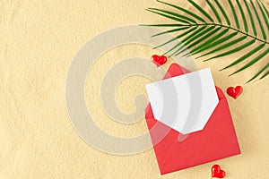 Flat lay photo of open envelope with white card, tropical leaf, red hearts