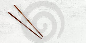 Flat lay photo - pair of dark wood chopsticks on white board. Wide banner for asian / chinese food, space for text on right