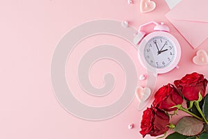 Flat lay photo of red roses, alarm clock, heart shaped candles and envelope